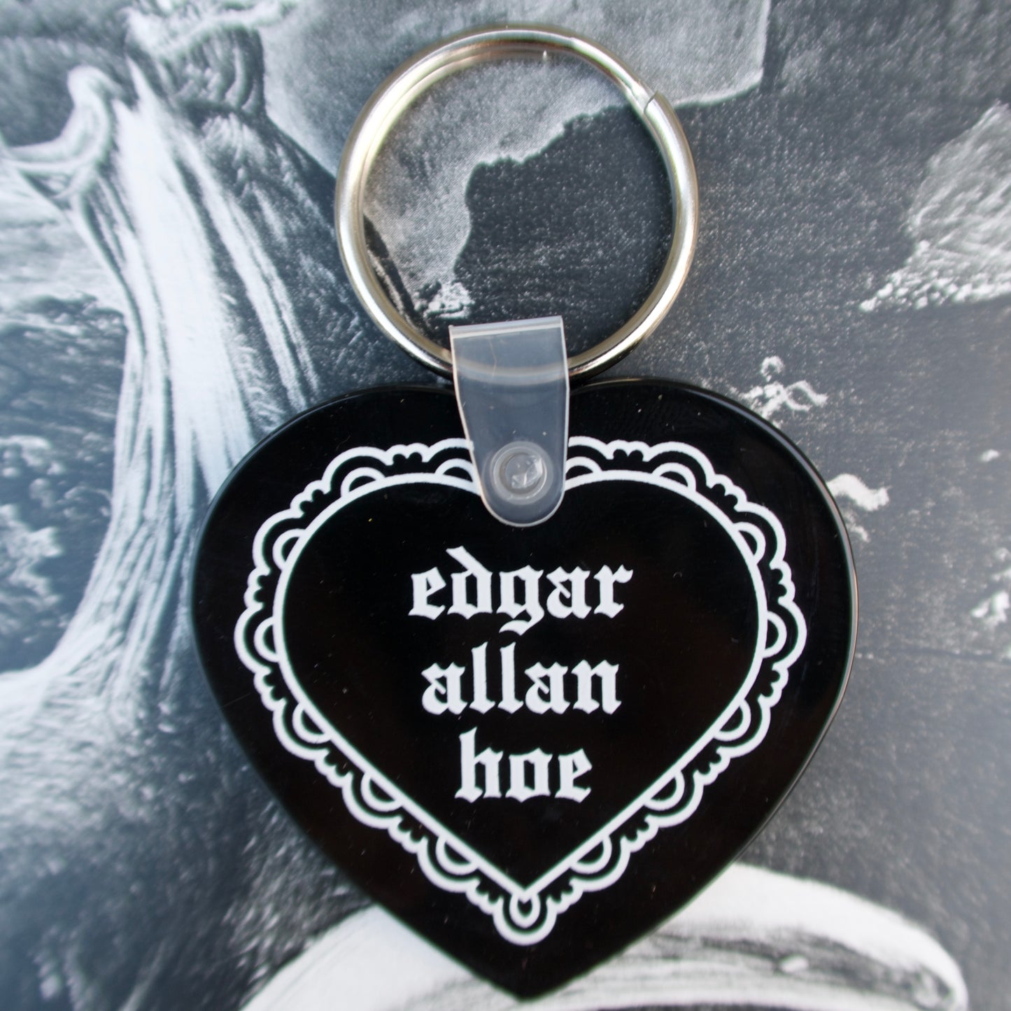 Heart-shaped keychain with 'edgar allan hoe' text on a black background